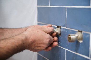 Tanınmayan yaşlı tesisatçı banyoya su musluğu kuruyor. Duş sistemini kurar.