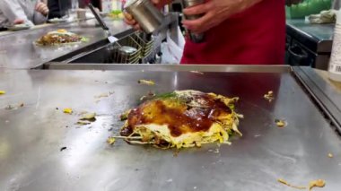 Yerel Hiroşima restoranında okonomiyaki pişiriyorum. Video 7. Aonori, dashi stok tozu ve yeşil soğanla çeşnili..