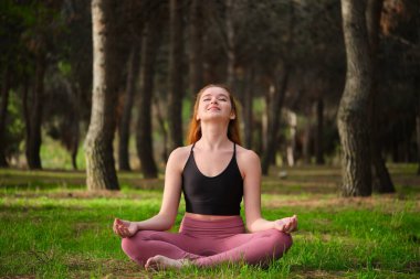 Kızıl saçlı genç kadın ormanda meditasyon yapıyor. Doğada meditasyon.