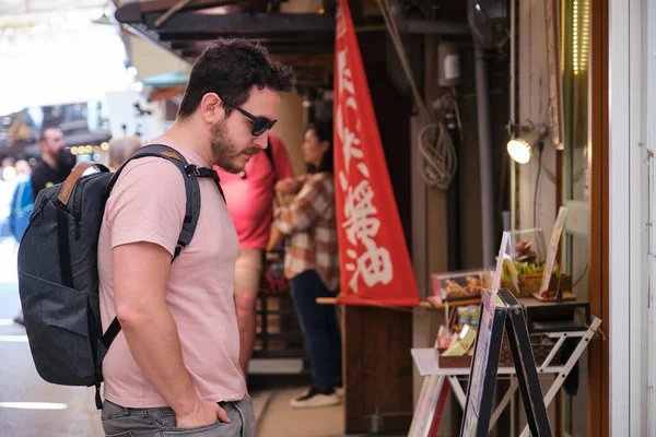 Miyajima, Hiroşima, Japonya 'da geleneksel bir caddede restoran menüsüne bakan Avrupalı turist.