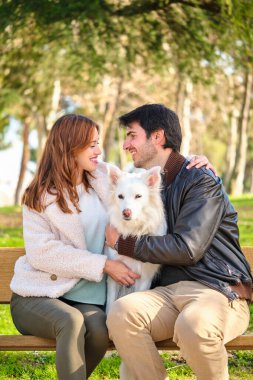 Kafkasyalı genç bir çift parktaki bankta köpekleriyle sarılıyorlar. Aile.