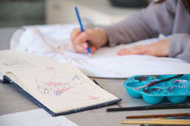 Tanımlanamayan bir kadın beyaz gömlekle bir tasarım yapıyor. Kadının yaratıcı ifadesi boyalı elbise tasarımları aracılığıyla.