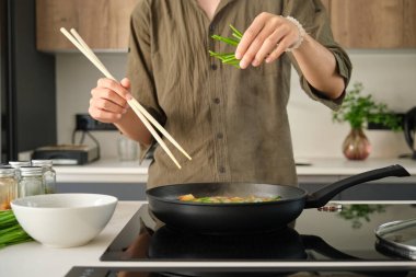 Close up of asian young man hands adding chive to prepare chinese or taiwanese tomato scrambled eggs at kitchen.