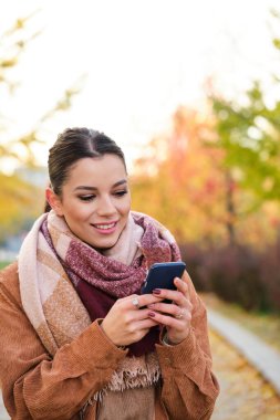 Sonbaharda gülümseyen telefonu kullanan beyaz bir kadın..