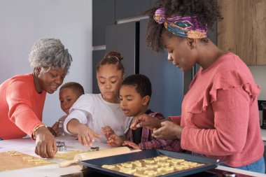 Afrikalı bir aile mutfakta kurabiye hamuru şeklinde kurabiye kesiyor. Yatay genişletilmiş aile.