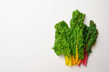 Bunch of rainbow swiss chard leaves on beige stone table. Top view of yellow, orange, red and green fresh swiss chards.