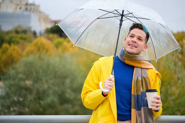 stock image Young man wearing a yellow raincoat with a coffee and umbrella in street in autumn.