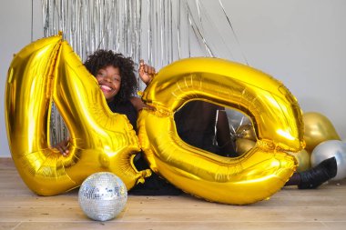 40 yaş günü partisinde Afrikalı bir kadın yerde 40 tane altın balonla oynuyor..