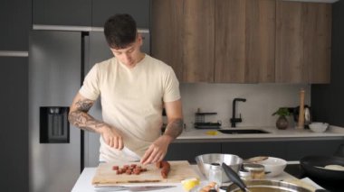Genç Ekvadorlu adam mutfakta yemek tarifi hazırlamak için sucuk kesiyor..