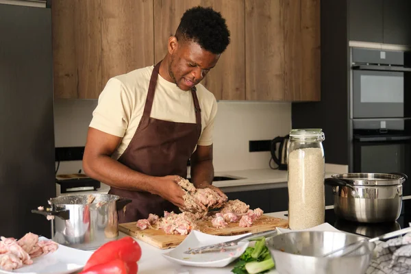 stock image Young african man preparing a chicken mince recipe in a kitchen.