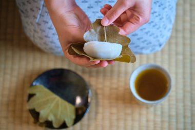 Japon Kashiwa mochi 'si ve tatami üzerinde yeşil çay tutan eller. Meşe yaprağıyla sarılmış kırmızı fasulye ezmeli Japon mochi 'si. Japon tatlıları..