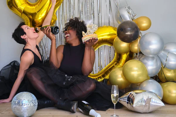 两名多种族妇女参加了一个40岁生日聚会 笑着喝着瓶子里的香槟 — 图库照片