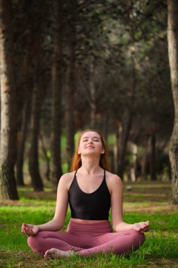Kızıl saçlı genç kadın ormanda meditasyon yapıyor. Doğada meditasyon.