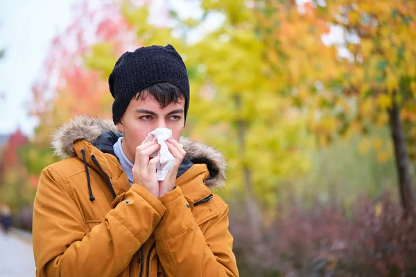 コート 手袋の若い男が通りで寒い秋の日にティッシュを使って鼻を吹いて — ストック写真