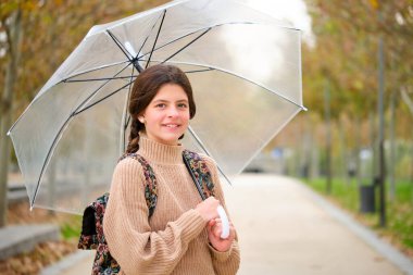 Preteen girl with an umbrella and backpack smiling and looking at camera outdoors in autumn. Back to school.