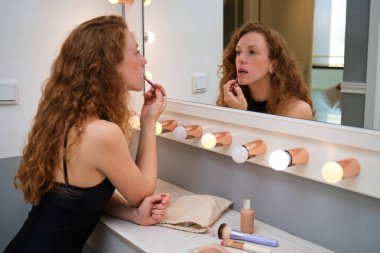 Young ballerina applying lipstick make up in front of the mirror.