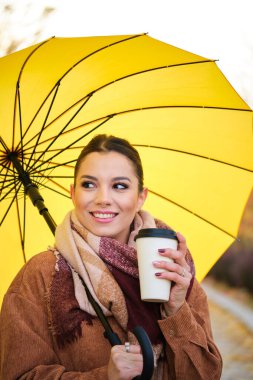 Sonbaharda kahve ve sarı şemsiyeli beyaz bir kadın gülümsüyor..
