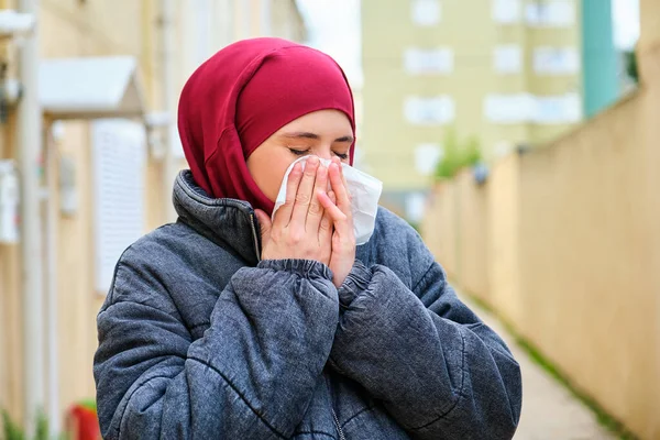 ヒジャーブのイスラム教徒の若い女性の肖像画とコートが通りの組織で彼女の鼻を吹いて — ストック写真
