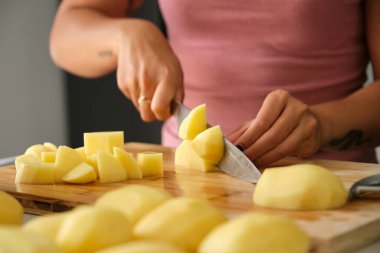 Tarifini hazırlamak için mutfakta patates kesen tanınmamış, genç, dövmeli Latin kadın..