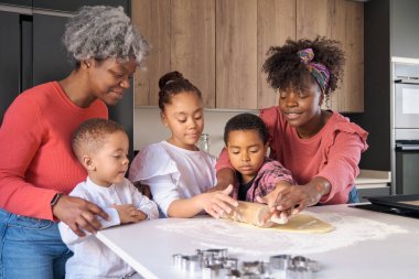 African happy family roll cookie dough out with a rolling pin in the kitchen. Horizontal extended family.