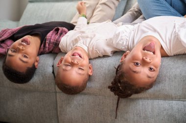 Üç çocuk kanepede baş aşağı oynuyor, birlikte eğleniyor ve eğleniyorlar..