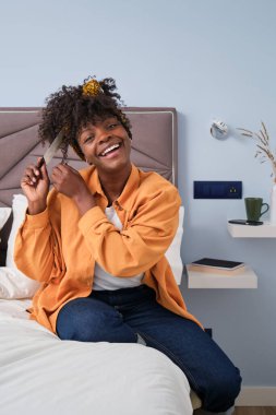 Gülümseyen Afrikalı genç bir kadın kıvırcık saçlarını tarıyor ve evde kameraya bakıyor..