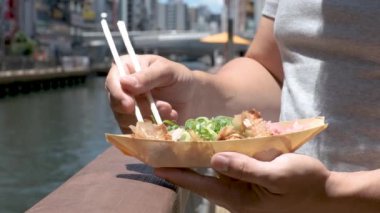 Japonya 'nın Osaka kentindeki Dotonbori Kanalı' nda takoyaki yiyen tanınmamış bir adam..