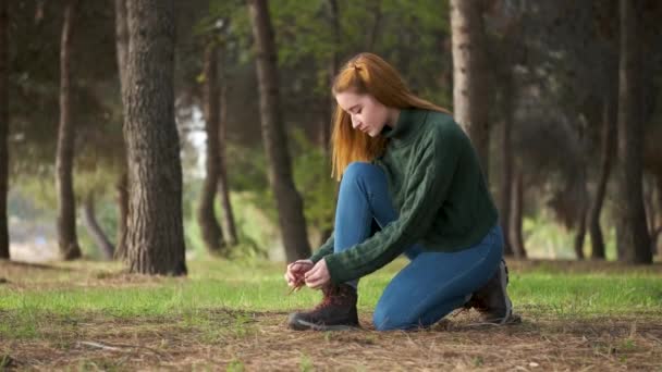 森の中でトレッキングブーツの靴を結ぶハイカーの赤毛の女性 — ストック動画