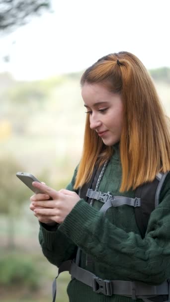 快乐的红头发女徒步旅行者一边徒步旅行一边看智能手机 远足的概念 — 图库视频影像