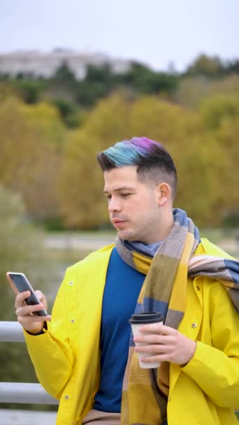 一个穿着黄色雨衣 头戴咖啡的年轻人在街上用智能手机 — 图库视频影像