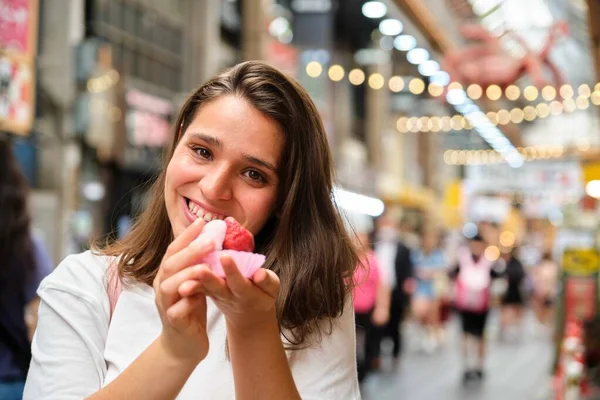 Tourist smiling and holding ichigo daifuku or strawberry mochi, soft and chewy mochi stuffed with fresh juicy strawberry and sweet red bean paste, at Osaka, Japan.