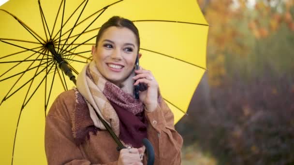 Biała Młoda Kobieta Podczas Rozmowy Telefonicznej Żółtym Parasolem Uśmiechnięta Jesienią — Wideo stockowe