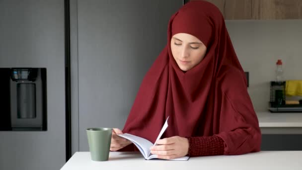 穿着头巾的穆斯林女青年在家里喝咖啡 在厨房看书 — 图库视频影像