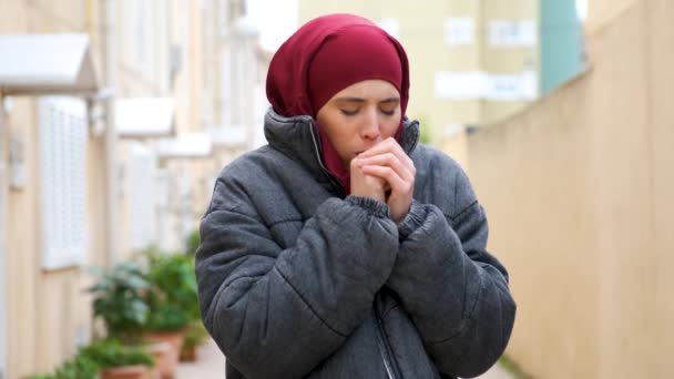 ヒジャーブのイスラム教徒の若い女性とコート暖かい手で息をし 咳をし 通りの組織で彼女の鼻を吹いて — ストック動画