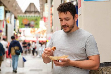 Japonya 'nın Osaka kentindeki Dotonbori caddesinde takoyaki yiyen Latin genç adam..