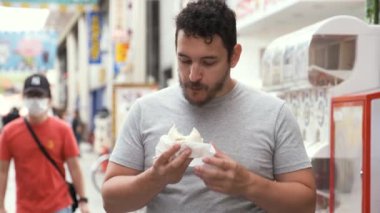 Latin genç adam nikuman yiyor ve Japonya 'nın Osaka kentindeki Dotonbori caddesindeki kameraya bakıyor..