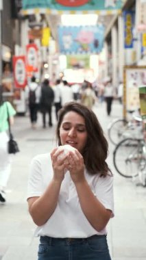İspanyol genç kadın nikuman yiyor ve Japonya 'nın Osaka şehrindeki Dotonbori caddesine bakıyor..