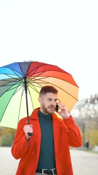 Latin Fiatalember Piros Kabátban Szivárvány Esernyővel Telefonál Utcán Ősszel — Stock videók