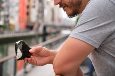 Onigiri yiyen tanınmamış bir adam, koni şeklinde beyaz pirinç topu, sokakta bir yaprak Norveç yosunuyla sarılı..