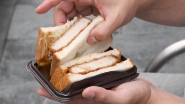 Tanınmayan kişi Katsu Sando yiyor, Japon sandviçi domuz pirzolası, lahana ve tonkatsu sosu yiyor, sokakta..
