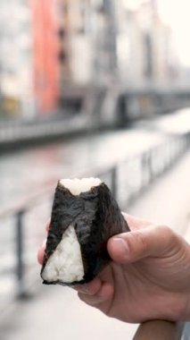 Onigiri yiyen tanınmamış bir insan, koni şeklinde beyaz pirinç topu, sokakta bir yaprak Norveç yosunuyla sarılı..