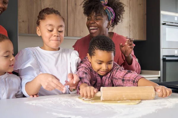 African family laughing while roll cookie dough out with a rolling pin in the kitchen. Horizontal extended family.