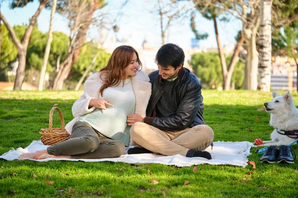 Man and pregnant woman on a picnic with their dog in a park. Family.