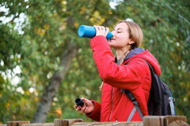 Genç bayan yürüyüşçü kantinden su içiyor. Ormanın manzarasını seyrediyor..