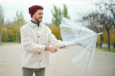 Genç adam şeffaf bir şemsiyeyi kapatıyor, sonbaharda sokakta yağmur durur..