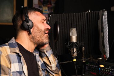 Kulaklık takan erkek şarkıcı mikrofonlu yeni bir single 'ı bir müzik stüdyosunda kaydediyor..