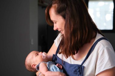 Annesinin kollarında emzik olan bir aylık beyaz bir kız. Bebek bakımı.