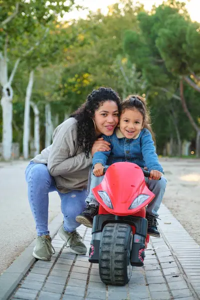 Happy Latin mother hugging her son on a balance bike in a park. Latin family.