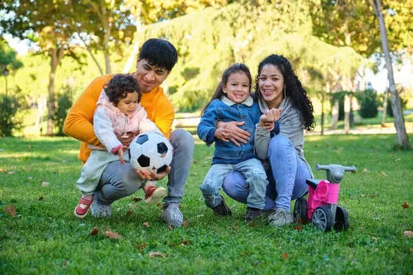 Latin family with two children soccer ball and balance bike in a park. Hispanic family.
