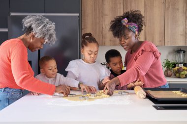 Afrikalı bir aile mutfakta kurabiye hamuru şeklinde kurabiye kesiyor. Yatay genişletilmiş aile.